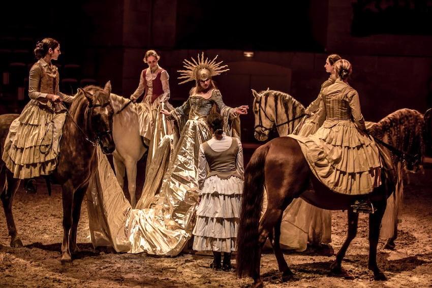 Tableau féerique d'un spectacle équestre de Noël aux Grandes Écuries de Chantilly : cavalières en costumes d'époque entourant un personnage vêtu d'or.